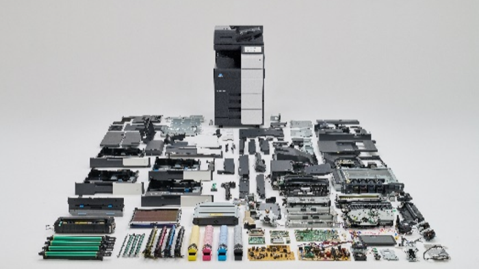 One multifunctional peripheral together with the many parts removed by dismantling it, including exterior sheet metal, circuit boards, toner cartridges and transport units, laid out across the floor
