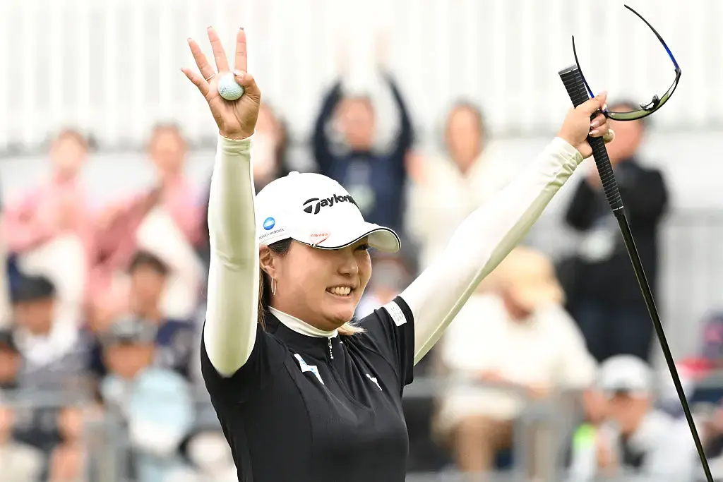 大会会場で、プロゴルフ選手・高橋彩華さんがボールを手に持ち、クラブを掲げている様子