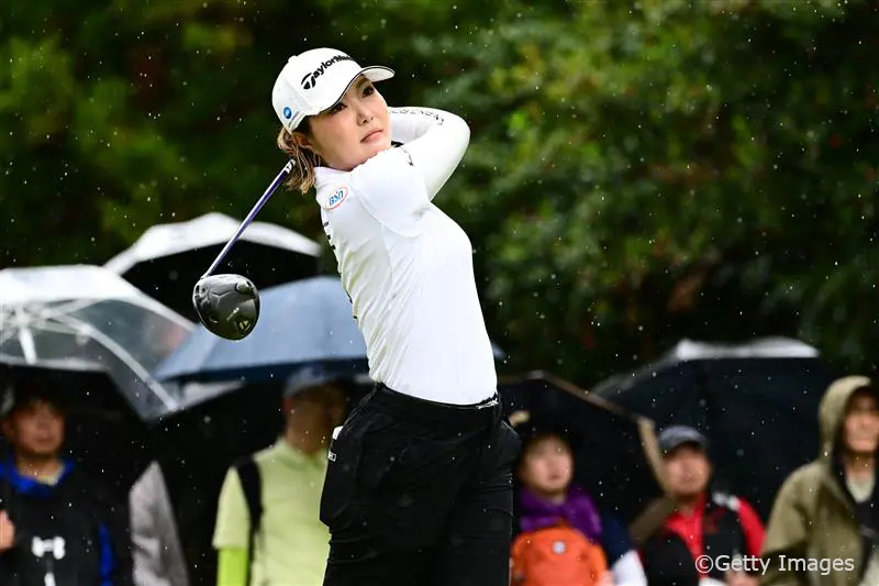 屋外ゴルフコースで白いウェアの高橋選手がスイングしている様子。背景には観客が写っている。