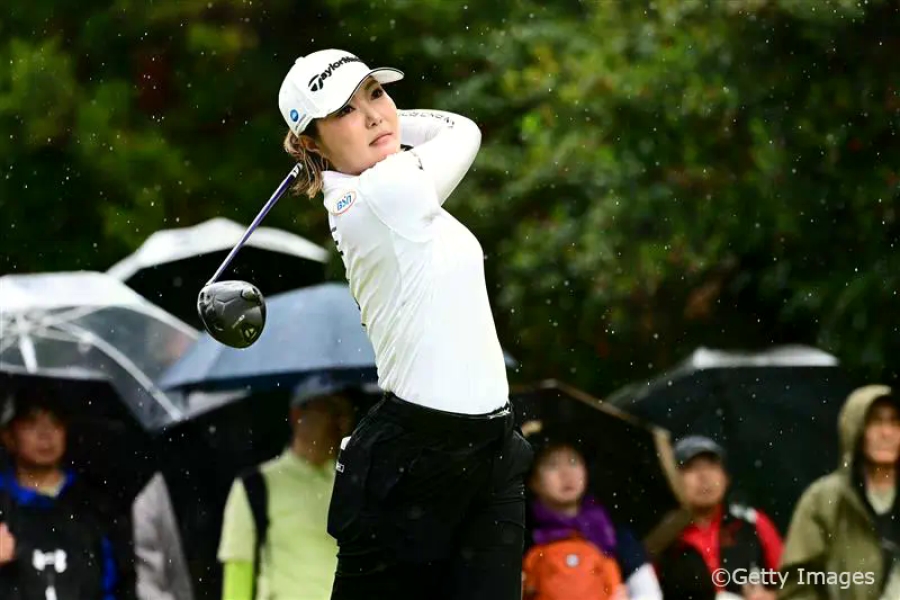 屋外ゴルフコースで白いウェアの高橋選手がスイングしている様子。背景には観客が写っている。