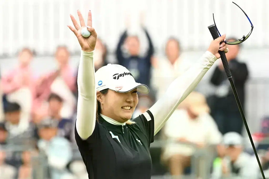 大会会場で、プロゴルフ選手・高橋彩華さんがボールを手に持ち、クラブを掲げている様子