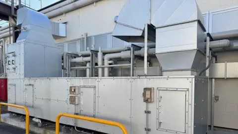 工場の屋外に設置された、ダクトが接続された銀色の大型気化式加湿器の外観写真