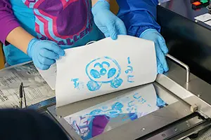 青い粉で描かれたパンダの絵を白い紙に写し取っている手元の写真