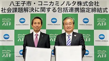 「八王子市・コニカミノルタ株式会社 社会課題解決に関する包括連携協定締結式」の看板を背に並ぶ両者の代表者
